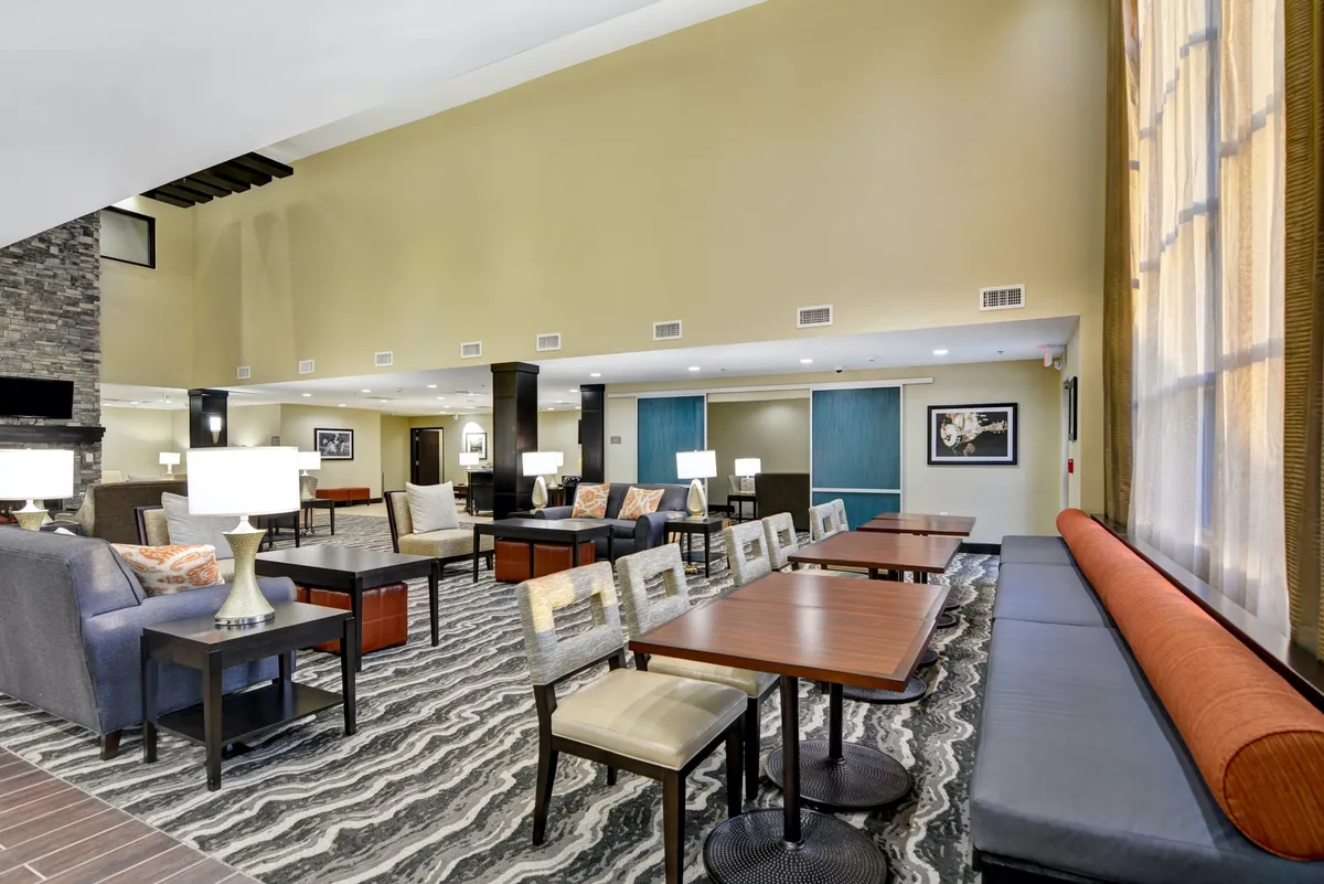 A modern living area with comfortable seating, contemporary lighting fixtures, a textured carpet, and tall windows with elegant drapery. The arrangement encourages conversation and relaxation, providing a harmonious blend of style and functionality.