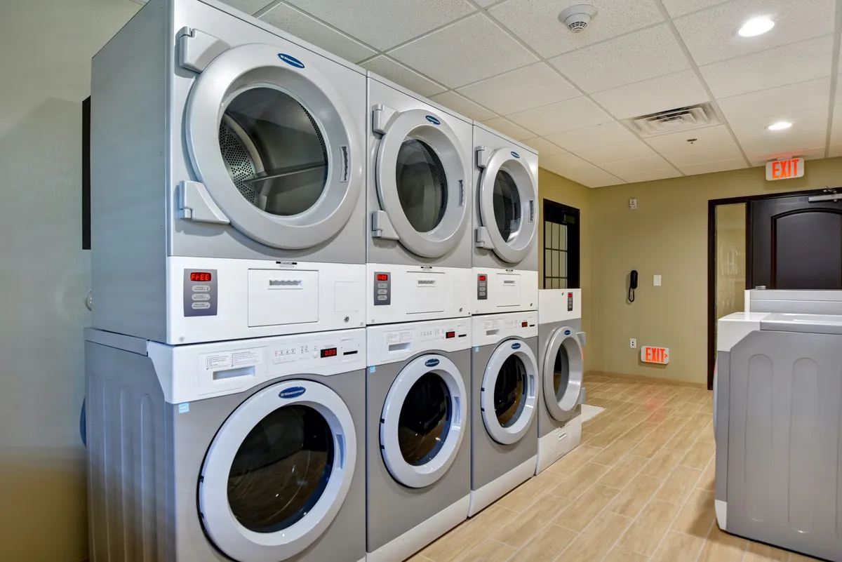 A practical laundry facility featuring stacked dryers, washing machines, and clear signage. The space is clean and functional, making longer stays more convenient for guests.