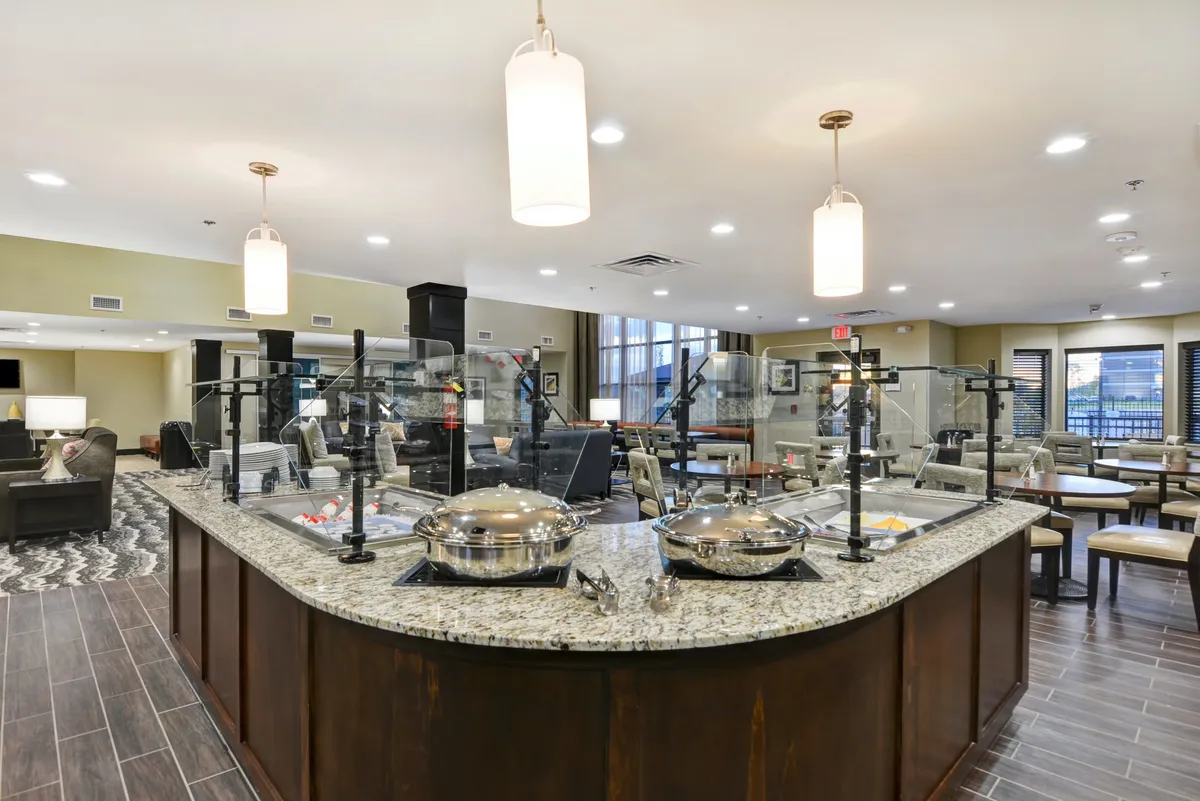 This image captures an inviting interior setting centered around a granite countertop, elegantly set with serving dishes and accented by stylish lighting fixtures. The layout hints at a space where guests gather for shared meals and casual celebrations, with an overall mood of warmth and sociability.