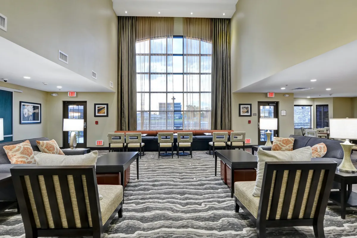 An inviting living room with large windows dressed in decorative curtains, stylish and spacious seating arrangements, modern coffee tables, and tasteful artwork. The abundance of natural light and open layout create a perfect setting for groups to gather, relax, or share stories in a comfortable atmosphere.