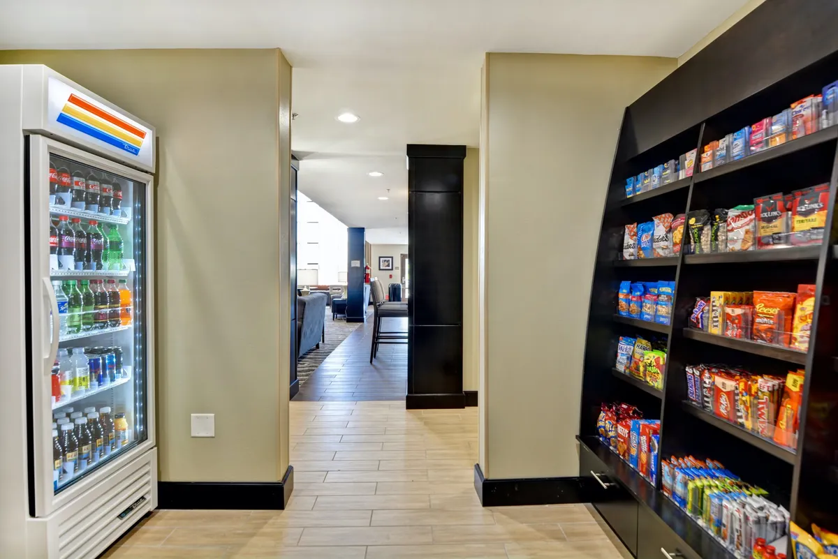 This image features a casual communal space with a vending machine, a snack shelf, and the reception in the background. The setting implies easy snack access and informal group interactions, reinforcing the relaxed, hassle-free vibe highlighted in the section.
