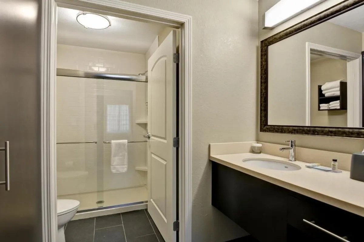 A modern, clean bathroom with a glass-enclosed shower, a sleek vanity counter topped with fresh towels, and a large mirror reflecting soft light. The space feels serene and inviting, designed for personal relaxation and daily routines.