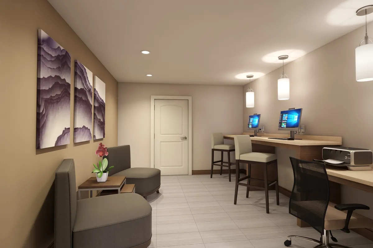 An inviting business center with computer stations, comfortable seating, and creative artwork on the wall. The space is designed for productivity and casual work, with a relaxed ambiance.
