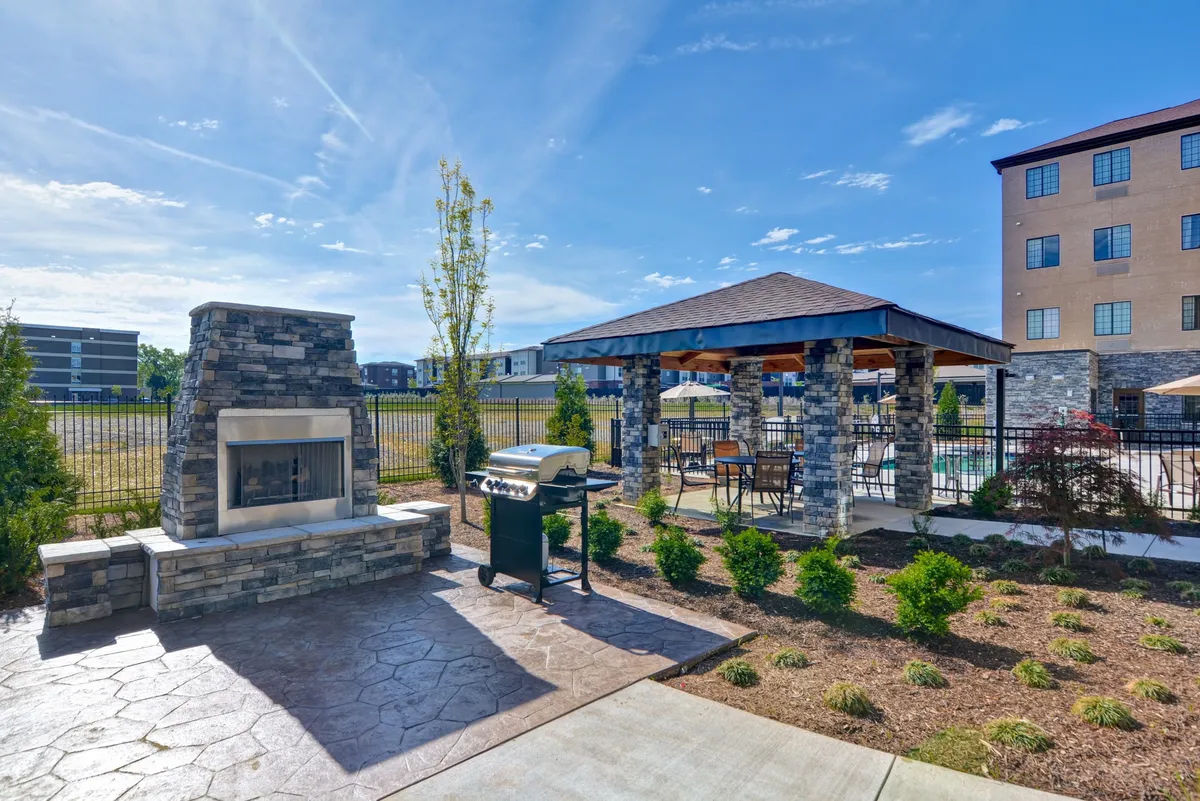 An exterior scene featuring a stylish stone fireplace, a grill, a gazebo, and a landscaped garden. The setup suggests a space for outdoor meals, social gatherings, and relaxing moments, ideal for families enjoying dinners together after a fun-filled day.